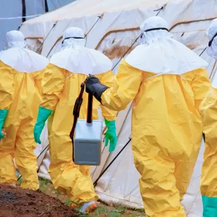 Red Cross volunteers in full protective equipment carry equipment toward a tent structure during Ebola response operations in the Democratic Republic of the Congo.