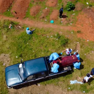 Aerial view of Red Cross volunteers in protective equipment carrying out a safe and dignified burial, with a coffin visible on a vehicle, during Ebola response operations in the Democratic Republic of the Congo.