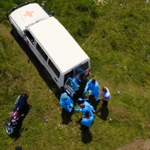 Aerial view of Red Cross volunteers in blue protective equipment gathered beside a marked Red Cross vehicle during Ebola burial and response operations in the Democratic Republic of the Congo.